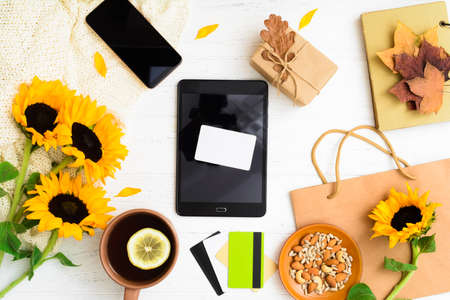 Empty bank card on tablet with gift, sunflowers, leaves, bag and tea with nutsの写真素材