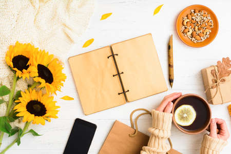 Autumn flat lay with notebook, tea with female hands, phone, nuts, gift on tableの写真素材