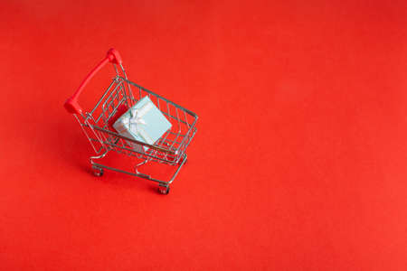 Shopping cart on wheels with gift box on red backgroundの写真素材