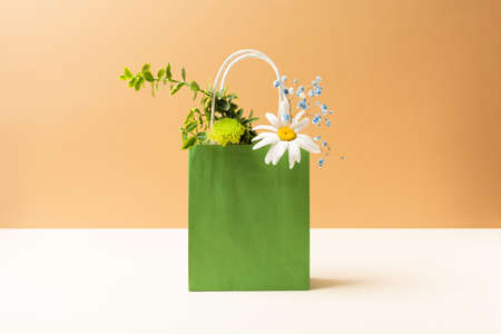 Paper bag with beautiful summer garden flowers and plants on beige backgroundの写真素材
