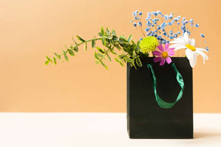 Paper bag with beautiful summer garden flowers and plants on beige backgroundの写真素材