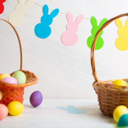 Many colorful Easter eggs in wicker basket with paper bunnies garlandの写真素材