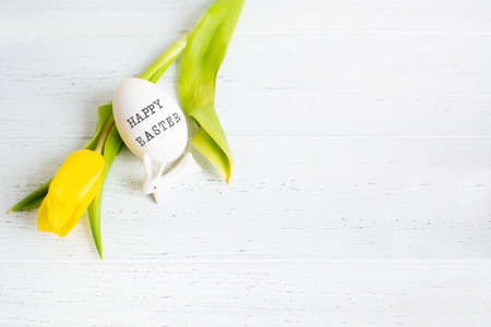 One egg with text Happy Easter and yellow tulip and white small ceramic bunnyの写真素材