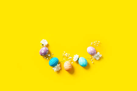 Easter flat lay composition with colorful painted eggs and flowers on yellowの写真素材
