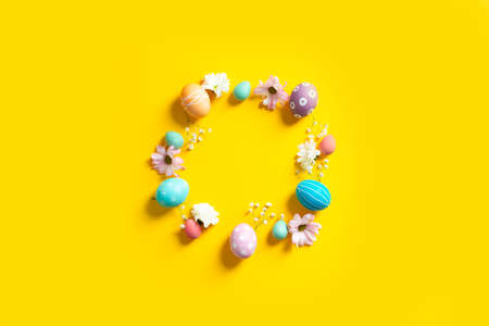 Circle of colorful painted natural eggs with flowers on yellowの写真素材