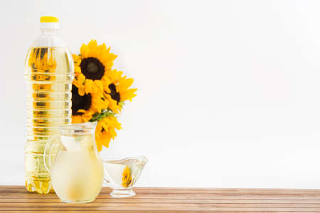 Plastic bottle and glass jars with sunflower oil and bouquet on wooden tableの写真素材