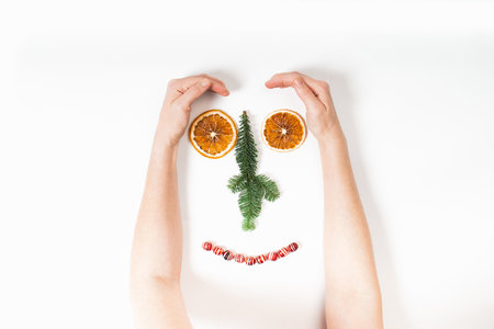 Funny face of Womans hands and Christmas decorations with dry orange, fir tree and candies on whiteの写真素材