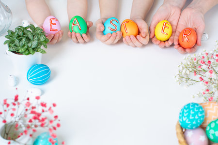 Colorful Easter eggs in hands with text. Holiday flat lay with copy spaceの写真素材