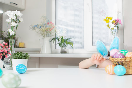 Holiday Easter background with spring flowers, colorful eggs and childs head with bunny ears and empty tableの写真素材