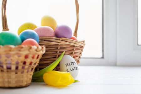 Wicker baskets with bright colorful eggs and with text Happy Easter and flowerの写真素材