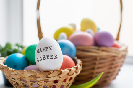 Wicker baskets with bright colorful eggs and with text Happy Easter and flowerの写真素材