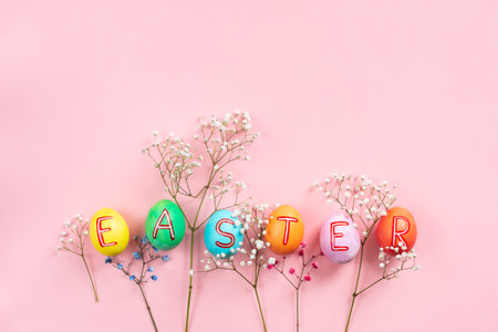 Easter flat lay composition with colorful painted natural eggs with text Easter on them and flowersの写真素材