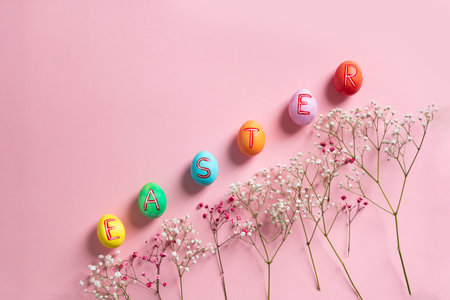 Easter flat lay composition with colorful painted natural eggs with text Easter on them and flowers