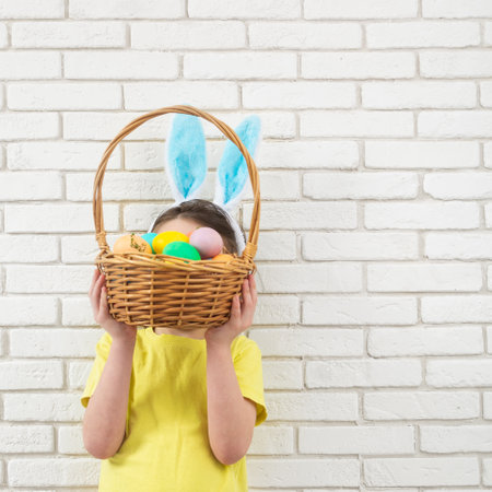 Boy with Easter bunny ears with wicker basket with colorful eggs. Copy spaceの写真素材