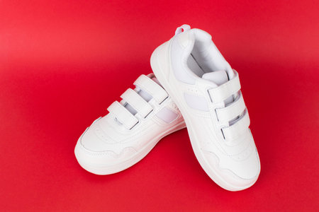 White children's sneakers on red background. Minimal background. Fashion blog or magazine concept. Advertisement for sale or shopの写真素材