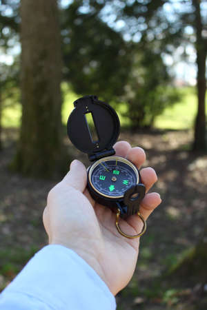 Male hand holding compass in forest, vertical orientation