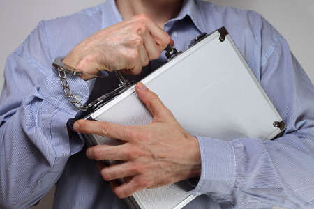 Businessman firmly holding a metal briefcase handcuffed to his wristの写真素材