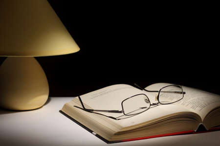 Reading glasses resting on top of open book next to night lampの写真素材