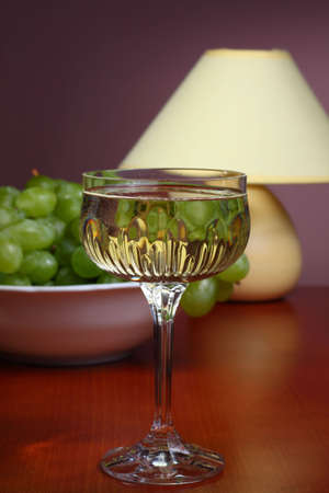Glass of white wine on wooden table with bowl of grapes and table lampの写真素材