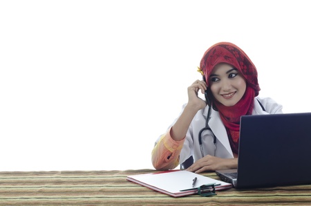 beautiful young muslim woman doctor with stylish head scarf make a phone call in front of laptop isolated on white backgroundの写真素材
