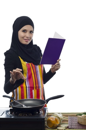 Beautiful muslim woman holding cook book to prepare cooking healthy food in the kitchenの写真素材