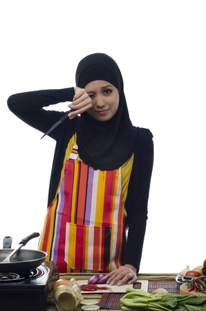 Beautiful muslim woman burning her eyes when cutting the onions and red peppers in the kitchenの写真素材