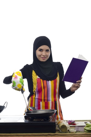 Beautiful muslim woman holding cook book during cooking healthy food in the kitchenの写真素材