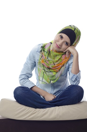 beautiful muslim woman with stylish head scarf sitting with cross-legged on a couchの写真素材