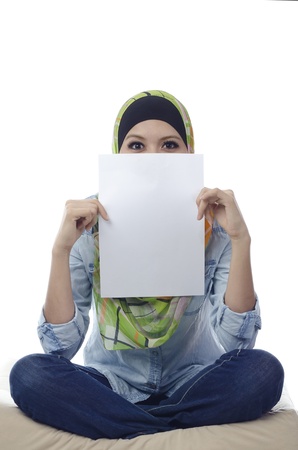 Beautiful young muslim woman seat and holding a blank paper.half face covered by blank paperの写真素材