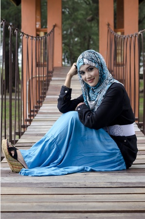beautiful young muslimah women with stylish head scarf smiling sit on the hanging bridge at recreation parkの写真素材