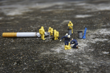 Miniature figures working in industrial - Close up of Hazardous Material (HAZMAT) personnel helping his colleague wearing protective clothing with background half cigarette on the floor.の写真素材