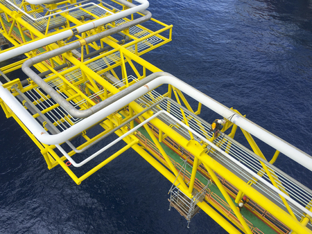 Oil and gas industry. View of oil and gas pipeline on the bridge and pipeline rack while a commercial abseiler sitting on the structure working at height and overboard in the middle of the sea.の写真素材