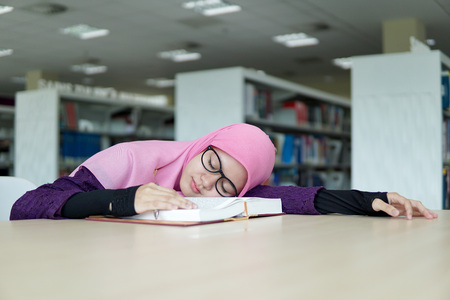 A beautiful Muslimah student holding a pen and sleeping on the book in the library           の写真素材