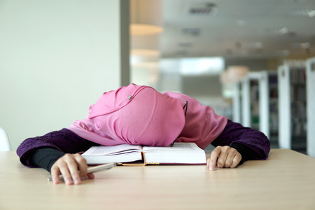 A beautiful Muslimah student holding a pen and sleeping on the book in the library.                    の写真素材