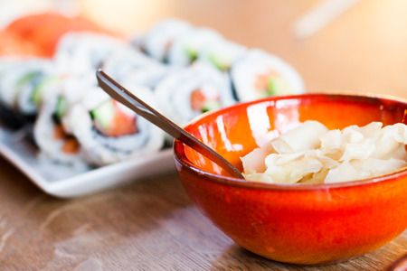 A big bowl with ginger gari and many rolls of maki California rolls in the background.の写真素材