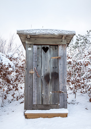 A wooden outhouse or privy in the Swedish winter, surrounded by snow. It has a heart on the door. Location: Amundon, Gothenburg, Sweden.の写真素材