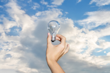 Hand Holding Lightbulb On Skyの写真素材