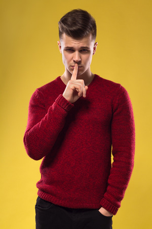 Handsome Man In Red Sweater Holding Finger To Lips In A Gesture For Silenceの写真素材
