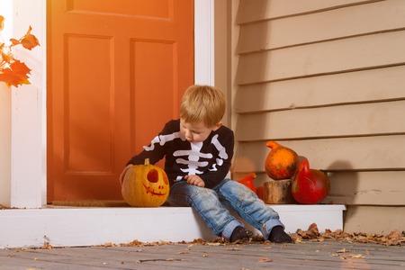 Little Boy Sits Near Halloween Pumpkin In The Courtyard. Halloween Themeの写真素材