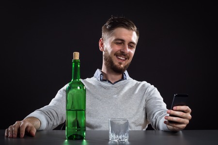 Drunk Man With Bottle Holding Mobile And Going To Make A Call On Black Backgroundの写真素材