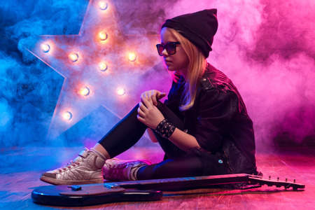 Little Rock Star Girl With Electric Guitar Sitting On The Floor On Smoke Backgroundの写真素材
