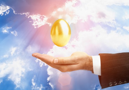Golden Egg Over Male Hand In A Business Suit On Sky Background. Gesture Signの写真素材