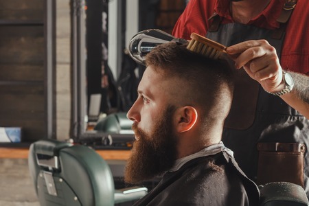 Serious Young Bearded Man Getting Groomed At Barber With Hair Dryer. Barbershop Themeの写真素材