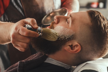 Serious Young Bearded Man Getting Beard Haircut By Barber. Barbershop Themeの写真素材