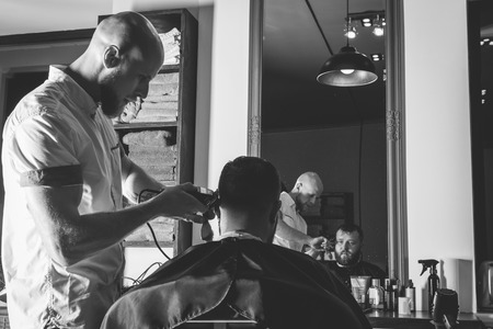 Serious Bearded Man Getting Haircut By Barber While Sitting In Chair At Barbershop. Barbershop Themeの写真素材