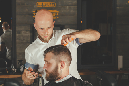 Serious Bearded Man Getting Haircut By Barber While Sitting In Chair At Barbershop. Barbershop Themeの写真素材