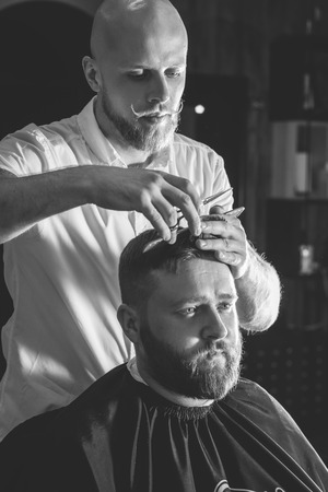 Serious Bearded Man Getting Haircut By Barber While Sitting In Chair At Barbershop. Barbershop Themeの写真素材