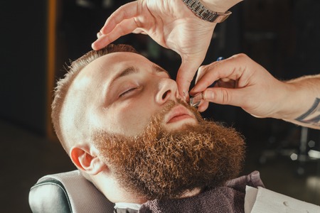 Young Bearded Man Getting Beard Haircut With A Straight Razor By Barber. Barbershop Themeの写真素材