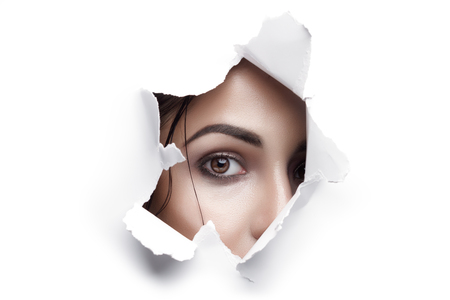 Woman With Brown Eyes Looking Through White Ripped Paper Holeの写真素材