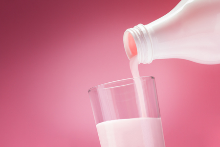 Pouring Yogurt From A White Bottle Into A Glass On A Pink Backgroundの写真素材